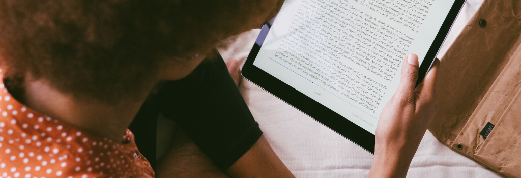 Woman sitting cross legged on bed reading an ebook