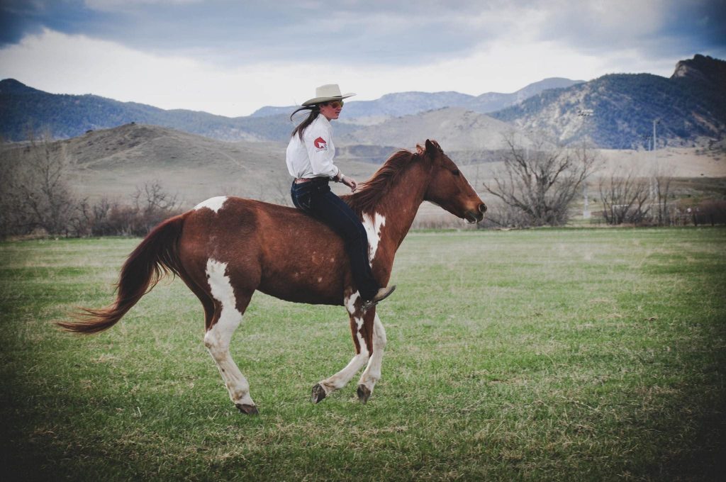 Margaret riding a horse across a large green field. There are mountains in the background.