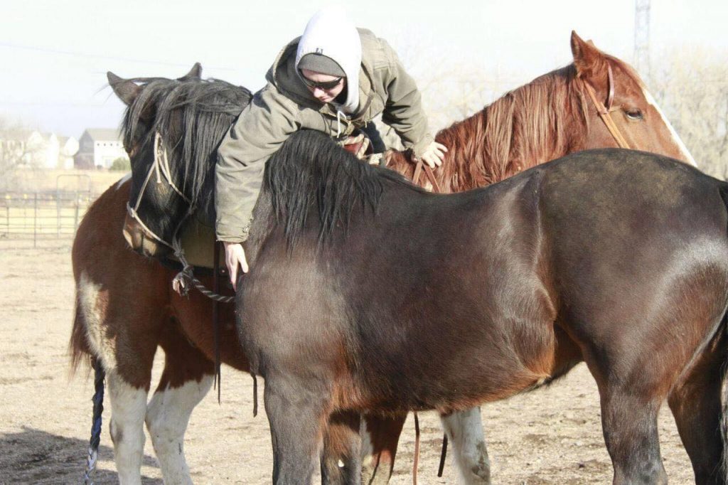 Margaret petting two brown horses. She is wearing a large jacket and hood.