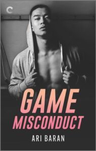 Cover image for Game Misconduct by Ari Baran, featuring a black and white photo of a man in an unzipped hoodie, looking right at the viewer. He is in a hockey locker room, and there are hockey sticks leaning against a wall in the background.