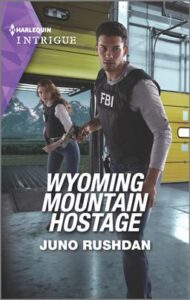 Cover image for Wyoming Mountain Hostage by Juno Rushdan, featuring a man in an FBI bullet proof vest. Behind him is a woman in a similar vest. They are walking through an empty warehouse.