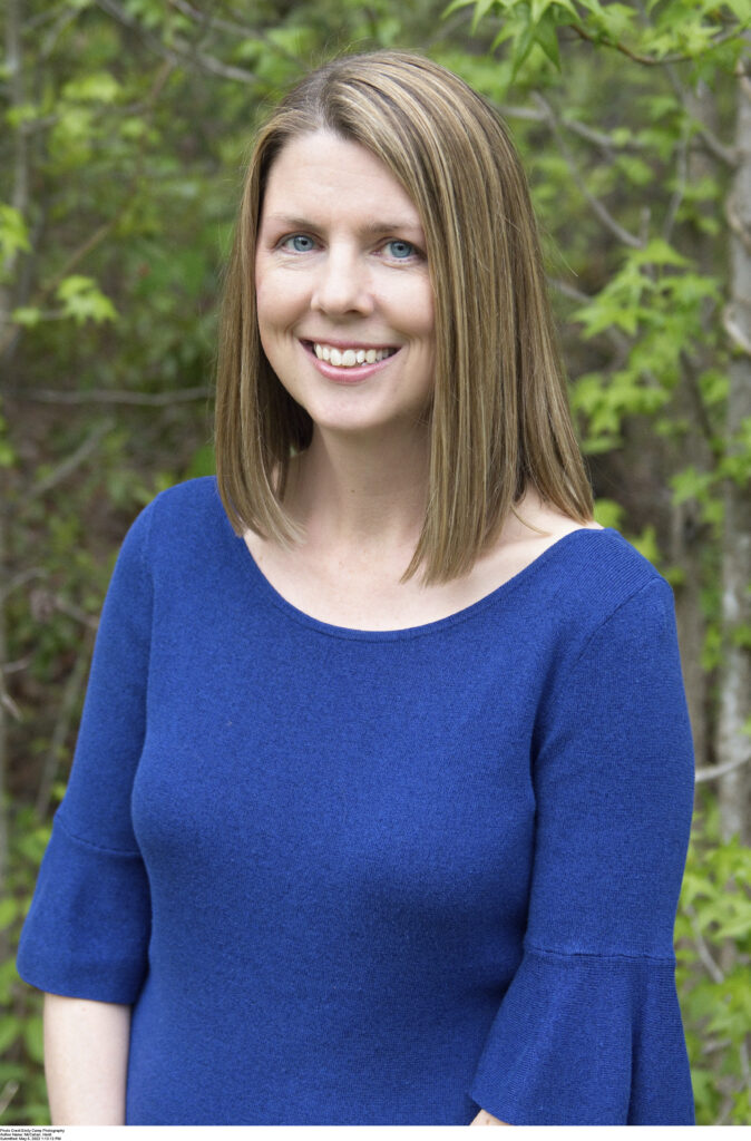 Image of author Heidi McCahan, a blonde woman standing outdoors with trees behind her, smiling at the camera