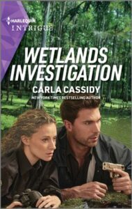 Cover image for Wetlands Investigation by Carla Cassidy, featuring a man and a woman crouching behind a log in the forest. The man is holding a gun. Both are looking into the distance, concerned.
