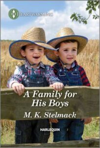 Cover image for A FAMILY FOR HIS BOYS by M. K. Stelmack, featuring two little boys in straw cowboy hats and overalls. They are standing in a field of wheat, behind a wooden fence.