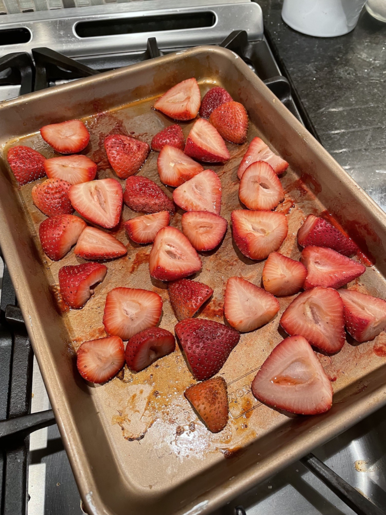 Image of cut up strawberries sitting on top of a counter. They have just been in the oven and are laid out in a sheet pan.