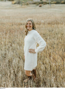 Image of author Jill Lynn, a woman in a white sweater dress standing in a field.