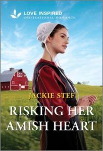 Cover image for Risking Her Amish Heart by Jackie Stef, featuring an amish woman in a field looking off to the right. Behind her is a large red barn.