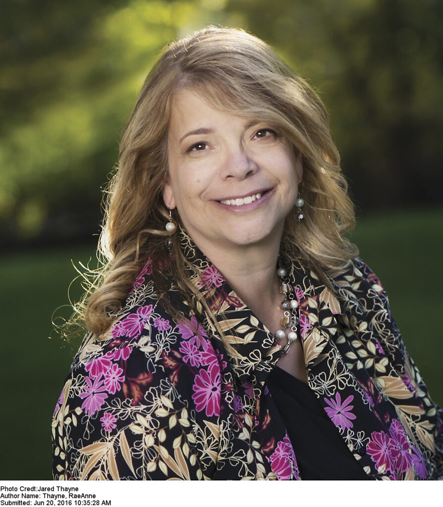 Image of author RaeAnne Thayne, a woman in a floral shirt sitting outside with trees behind her.