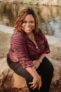 An image of Yahrah St. John, sitting on a rock by a stream.